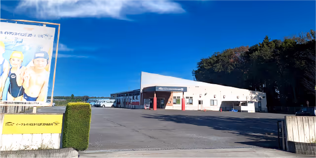 青空の下、広い駐車場の奥に白い建物が立っている屋外の施設。