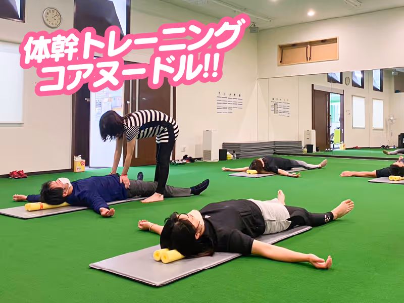 床に寝そべりながら体幹トレーニングを行う数人の人と指導するインストラクター。