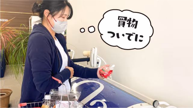 マスクを着けた女性が買い物かごを持ち、レジで商品を手に取っている様子。