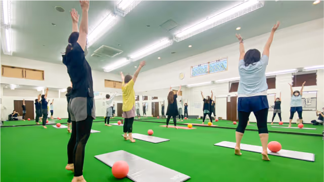 フィットネススタジオでマットとボールを使いながら腕を上げてストレッチする複数の女性たち。