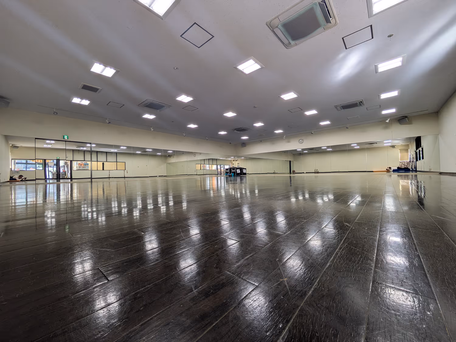 広い木製フロアのダンススタジオ、壁一面に大きな鏡と天井の蛍光灯照明。