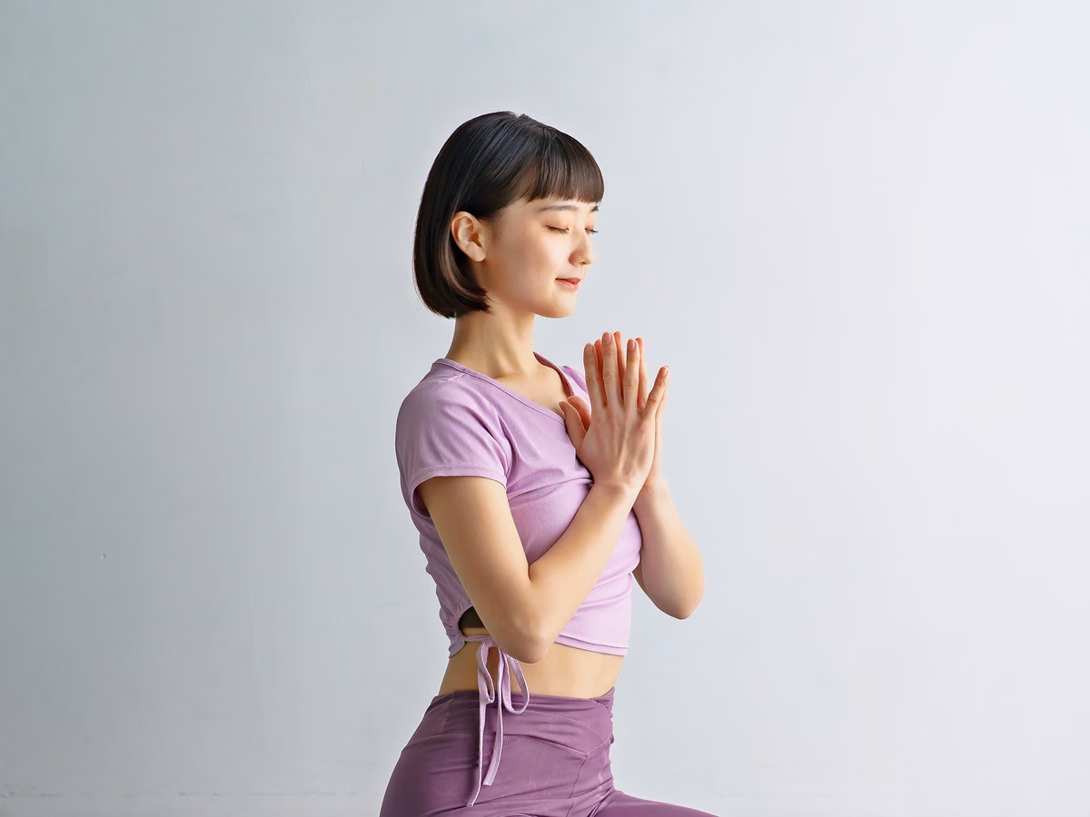 片膝立ちで胸の前に手を合わせる女性。