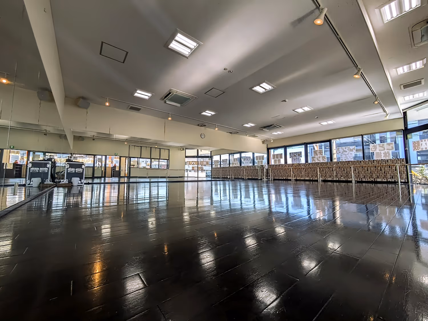 広くて照明が明るい鏡張りの壁と黒光りする床が特徴のダンススタジオ。